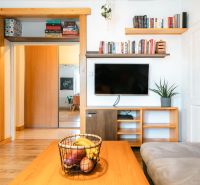 Living room with a TV, books, and fruit on the table, a 3-room apartment with wood-patterned flooring.