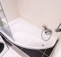 Bathroom with a bathtub, shower screen, and washing machine in a 3-room apartment.