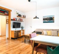 Living room in a 3-room apartment with a wooden decor floor, comfortable sofa, and television.