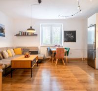 Living room with wood-patterned flooring, a sofa, and a dining table in a three-room apartment.