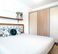 A bedroom with a bed, built-in wardrobe, and wooden decor flooring in a three-room apartment.