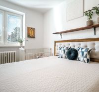 A bright bedroom with a bed, decorative pillows, plants, and a window in a three-room apartment.