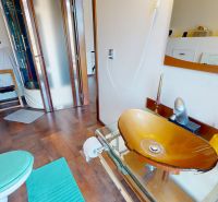 A bathroom with a colored glass sink, a shower, and a wooden decor floor in a family house.