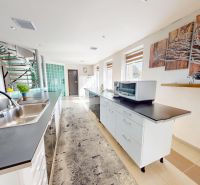 A kitchen in a family house with a long countertop, a sink, and stairs.