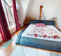 Bedroom in a family house with a large window, bed, and floor with wooden decor.