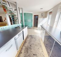 A kitchen in a family house with white cabinets and a staircase, glass bricks, and natural light.
