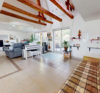 Living room in a family house with a beamed ceiling, piano, and fireplace.