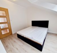 A bedroom in a three-room apartment with a wood-patterned floor and a simple bed.