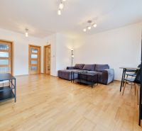 A room of a three-room apartment with a wooden decor floor, a gray sofa, and a table.