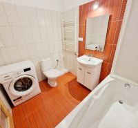 A bathroom in a 3-room apartment with a shower, a washing machine, and orange tiles.