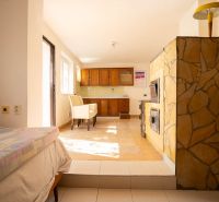 Interior in a family house with a fireplace, bed, kitchen cabinets, and table.