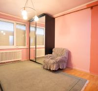 A room in a family house with a wooden decor floor, a mirrored wardrobe, and an armchair.