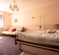 A bedroom in a family house with a carpet, bed, sofa, and chandelier.