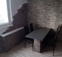 Dining area with a table and chairs in a 2-room apartment, stone wall.