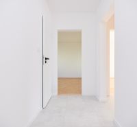 A hallway in a 3-room apartment with white walls and a floor with a wood decor.