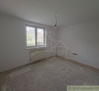 An empty room with a plastic window, a radiator, and an exposed ceiling light in a family house.