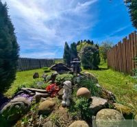 The garden of a family house in Mýtna with trees, a sculpture, and a wooden fence.