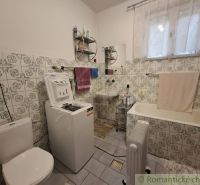 A bathroom in a family house with a washing machine, a bathtub, and tiles with a floral pattern.