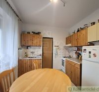 A kitchen in a family house with wooden cabinets, a dining table, a refrigerator, chairs.