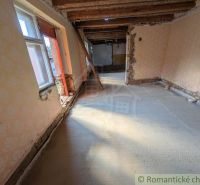 The interior of a family house with exposed wooden ceilings and damaged walls.
