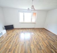 A spacious living room with a wooden decor floor and a large window in a 3-room apartment.