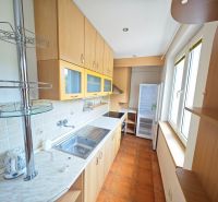 A kitchen in a 3-room apartment with a cooktop, cabinets, and windows, and a floor with a wooden decor.