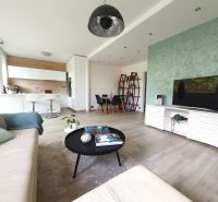 Living room with wood-patterned flooring, open space, and kitchen in a 3-room apartment.