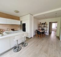 A kitchen with a dining area, white cabinets, and a wood-patterned floor in a three-room apartment.