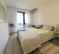 A bright bedroom with wood-patterned flooring in a three-room apartment.