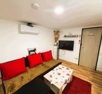 A living room in a cottage with a wood-patterned floor and red accessories.