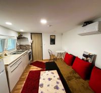 Interior of a cottage with a kitchen, red cushions, and a wooden decor floor.