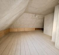 Attic space in a family house with a floor featuring a wooden decor and an unfinished ceiling.