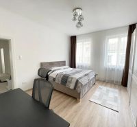 A bright bedroom with wood-patterned flooring and a desk in a three-room apartment.