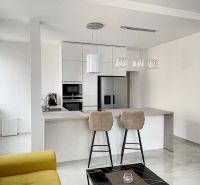 A kitchen in a 3-room apartment with an island, bar stools, and light cabinets.