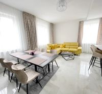 A bright living room with a dining table, a yellow sofa, and bar stools in a three-room apartment.