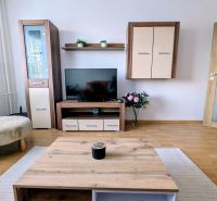 Living room of a two-room apartment with a wooden decor floor and TV furniture.