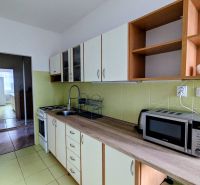 A kitchen in a 2-room apartment with a microwave and a stovetop, leading into another room.