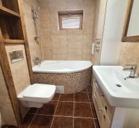 A bathroom in a 2-room apartment with a bathtub and cabinets, light brown tiles and flooring.
