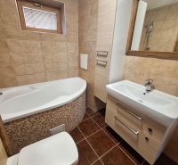 A bathroom with a corner bathtub, sink, and toilet in a 2-room apartment.