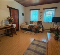 A room with a sofa, wooden decor flooring, flowers, and a table in a family house.
