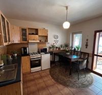 A kitchen in a family house with wooden cabinets and a dining table surrounded by plants.