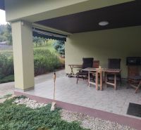 The terrace of a family house in Trebostovo with wooden garden furniture and landscaped greenery.