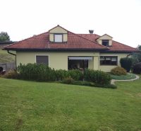 A family house in Trebostovo with a red roof surrounded by green lawn and shrubs.