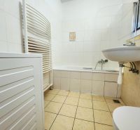 A bathroom in a 2-room apartment with a bathtub, sink, and washing machine, tiled with white tiles.