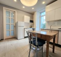 A kitchen in a 2-room apartment with a wooden decor floor, white cabinets, and a window.