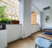 A balcony in a 2-room apartment with flower pots and wooden furniture.