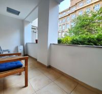 A balcony of a 2-room apartment with a view of greenery and a building, seating with chairs.