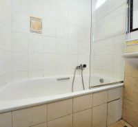 Bathroom in a 2-room apartment with a bathtub and a sink, tiled with light tiles.
