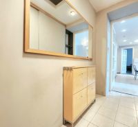 A hallway in a 2-room apartment with wooden furniture, tiles, and a large mirror.