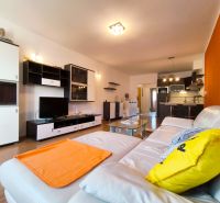 Living room in a 2-room apartment with a white sofa, orange accent, and a floor with a wood decor.
